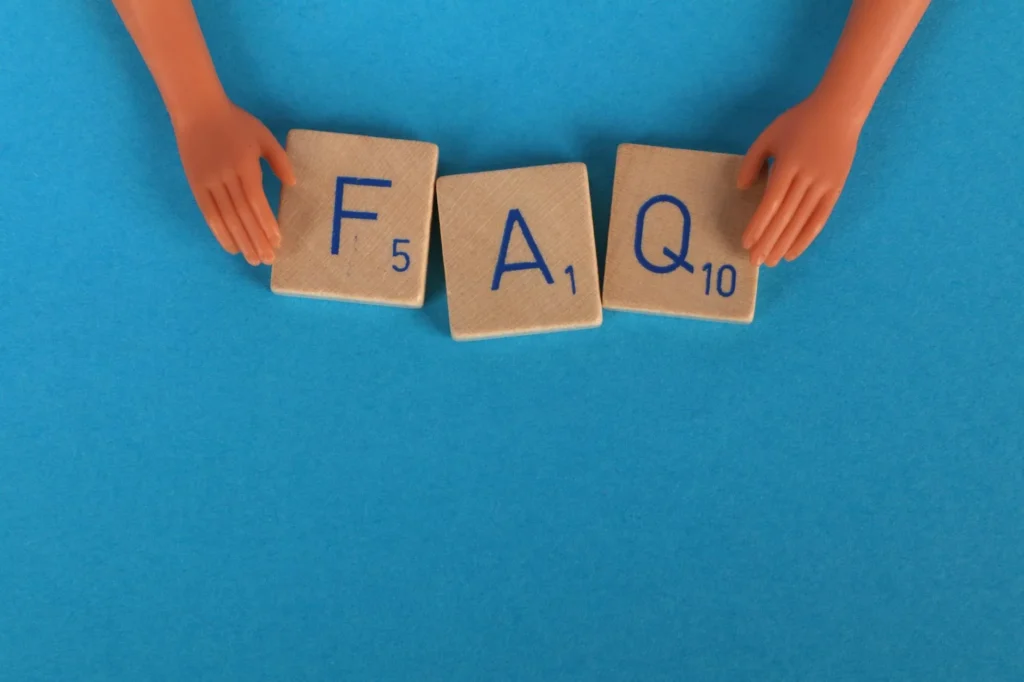 Flat lay of scrabble tiles spelling 'FAQ' with toy hands on a blue background, creating a conceptual
