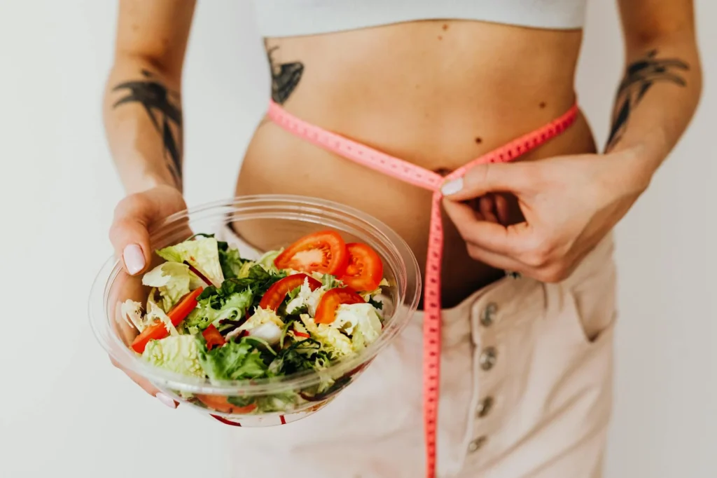 酵素果凍減肥真的有效嗎?正確吃法、功效與選購完整指南 8 Woman holding vegetable salad and measuring waist with tape, symbolizing healthy lifestyle choices.